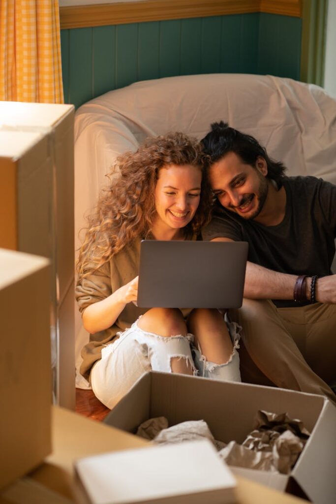 pexels-photo-4247819 Smiling couple using laptop while unpacking boxes in their new home. Bright, cozy indoor setting perfect for relocation themes.